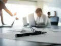 Okulary i długopis na dokumentach, w tle pracownicy analizują nowy kodeks pracy.