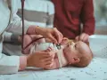 Pielęgniarka środowiskowa po porodzie osłuchuje noworodka. Rodzice obserwują badanie.