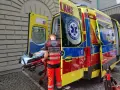 Ratownik medyczny ładuje pacjenta na noszach do karetki. Na jego kamizelce widnieje napis "RATOWNIK MEDYCZNY".
