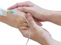 Dwie dłonie, jedna z wenflonem, druga trzymająca ją czule. Jak podłączyć kroplówkę instrukcja krok po kroku.