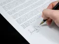 Podpisanie aneksu do umowy. Dłoń z piórem wiecznym składa podpis na dokumencie.