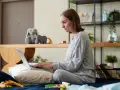 Kobieta w piżamie pisze na laptopie, przygotowując wniosek o urlop macierzyński. Obok pluszowy królik i zabawki.