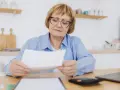 Kobieta w wieku 60 lat, po 40 latach pracy, z troską przegląda dokumenty dotyczące emerytury.