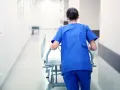 Salowa w niebieskim uniformie pcha łóżko szpitalne korytarzem. To część jej obowiązków w szpitalu.
