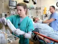 Ratownik medyczny i pielęgniarka pracują w szpitalu. Pacjent leży na łóżku, a personel medyczny monitoruje jego stan.