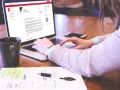 Kobieta pisze list motywacyjny bez doświadczenia na laptopie, obok kubek kawy i notatki.