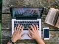 Ręce piszą CV funkcjonalne na laptopie, obok leży otwarta książka i telefon.