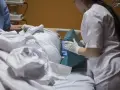 Asystent pielęgniarki, wykonując swoje uprawnienia, pomaga pacjentowi w łóżku, podkładając poduszkę.