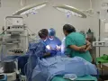 Zespół medyczny, w tym pielęgniarka zabiegowa, pracuje przy pacjencie na stole operacyjnym.