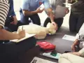 Uczestnicy kursu resuscytacji ćwiczą na fantomie. Jedna osoba notuje, instruktor pokazuje technikę.