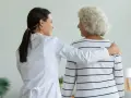 Opiekunka medyczna z troską obejmuje starszą panią. Empatia i wsparcie to kluczowe cechy opiekuna medycznego.