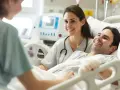 Uśmiechnięty pacjent w szpitalu rozmawia z opiekunką medyczną. To pokazuje, jak podnieść kwalifikacje opiekuna medycznego poprzez empatię i profesjonalizm.