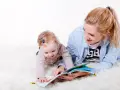 Uśmiechnięta opiekunka czyta książeczkę dziecku. To idealny przykład, jak wygląda praktyka na kursie opiekuna w żłobku.