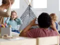 Opiekunka dziecięca z uwagą słucha opowieści małego chłopca, który siedzi obok namiotu tipi.