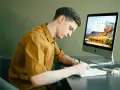 Student pracuje zdalnie, notując pomysły na komputerze. Idealna praca online dla studenta.