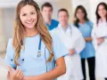 Uśmiechnięta pielęgniarka psychiatryczna z zespołem medycznym w tle. Trzyma tablicę z dokumentami.