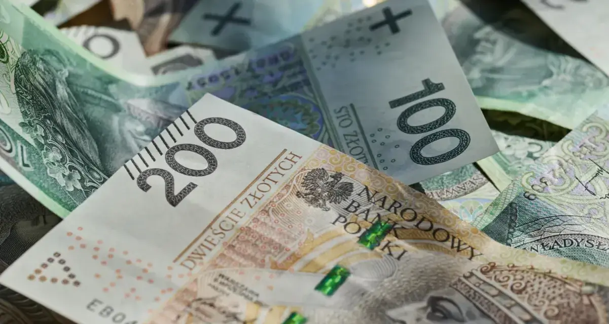 Złotówki, w tym banknot 200 zł, tworzą stos. Marzenia o wakacjach w 2026 roku? Trzynastka pomoże!