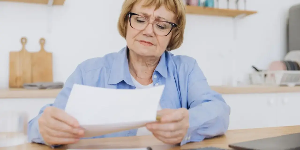 Kobieta w wieku 60 lat, po 40 latach pracy, z troską przegląda dokumenty dotyczące emerytury.