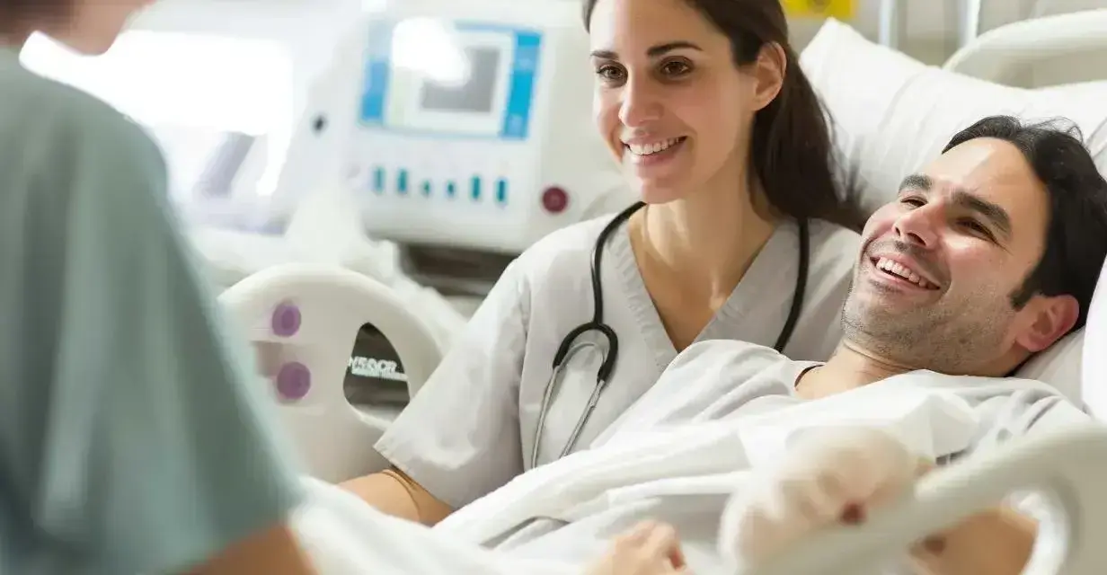 Uśmiechnięty pacjent w szpitalu rozmawia z opiekunką medyczną. To pokazuje, jak podnieść kwalifikacje opiekuna medycznego poprzez empatię i profesjonalizm.