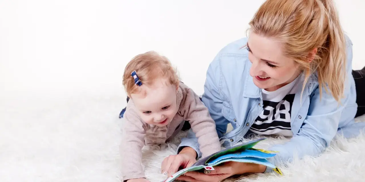 Uśmiechnięta opiekunka czyta książeczkę dziecku. To idealny przykład, jak wygląda praktyka na kursie opiekuna w żłobku.