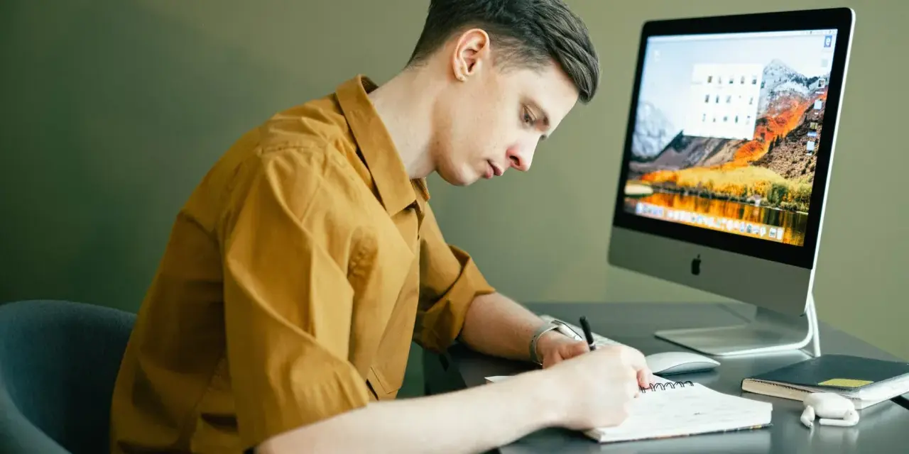Student pracuje zdalnie, notując pomysły na komputerze. Idealna praca online dla studenta.