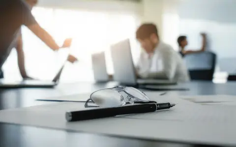 Okulary i długopis na dokumentach, w tle pracownicy analizują nowy kodeks pracy.