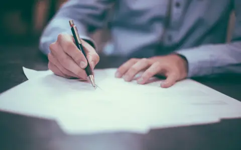 Dłoń pisze piórem na dokumencie, być może to akt porzucenie pracy.