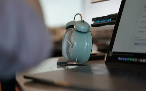Budzik obok laptopa przypomina o pracy. 3/4 etatu ile to godzin? Czas na efektywność!