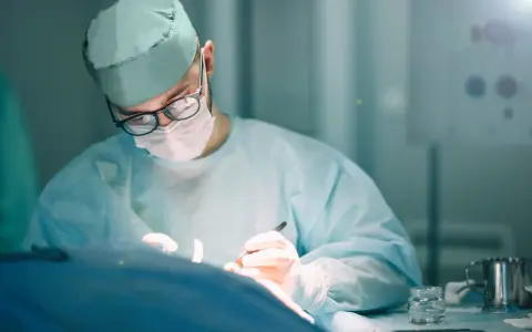 Chirurg w okularach i masce, w czepku i fartuchu, wykonuje precyzyjną specjalizację chirurgiczną.