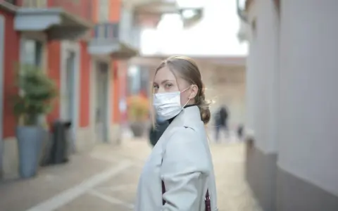 Kobieta w masce na twarzy, zastanawia się, ile można być na L4, spacerując ulicą.