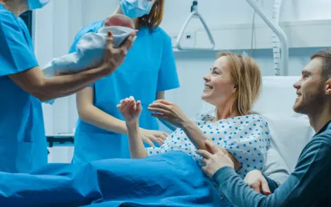 Szczęśliwi rodzice odbierają noworodka od położnej. Nauka i praktyka w najlepszym wydaniu, tworzą rodzinę.