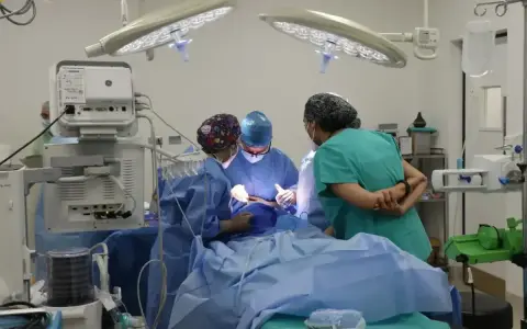 Zespół medyczny, w tym pielęgniarka zabiegowa, pracuje przy pacjencie na stole operacyjnym.