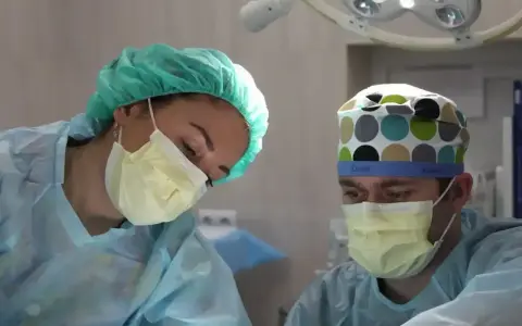 Dwie osoby w strojach chirurgicznych, jedna z nich to pielęgniarka, skupione na pracy. Zawód pielęgniarki wymaga precyzji i zaangażowania.
