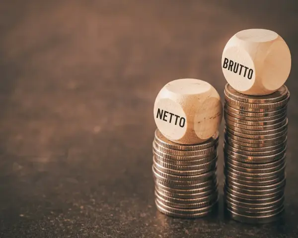 Dwie wieże monet, jedna z napisem "NETTO", druga z "BRUTTO". Symbolizują różnicę między zarobkami, pokazując, jak średnia krajowa netto różni się od brutto.