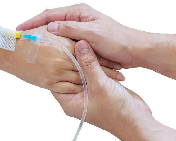 Dwie dłonie, jedna z wenflonem, druga trzymająca ją czule. Jak podłączyć kroplówkę instrukcja krok po kroku.