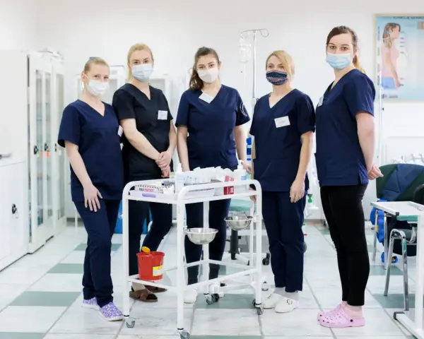 Pięć studentek pielęgniarstwa w granatowych uniformach i maseczkach stoi przy wózku medycznym. To ich przyszła praca dla studenta pielęgniarstwa.