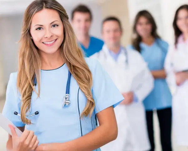 Uśmiechnięta pielęgniarka psychiatryczna z zespołem medycznym w tle. Trzyma tablicę z dokumentami.