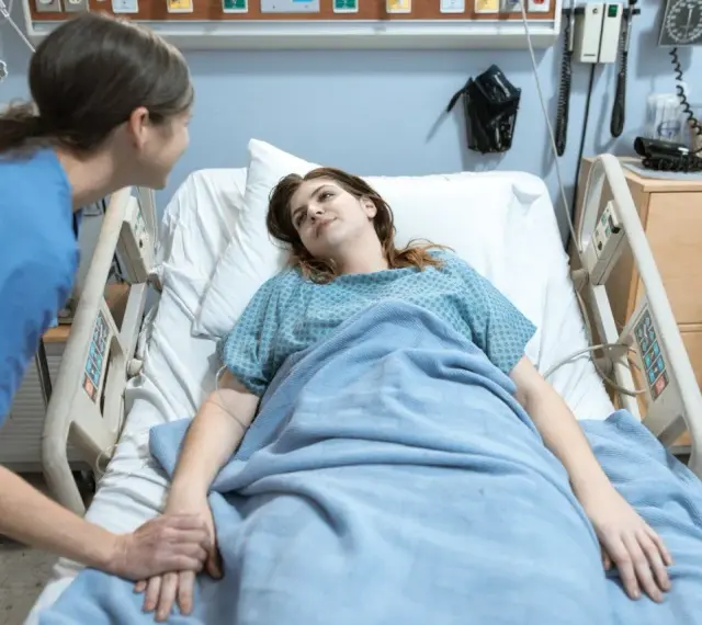 Pielęgniarka trzyma za rękę pacjentkę w szpitalnym łóżku. To jak list motywacyjny dla zdrowia, pełen nadziei.