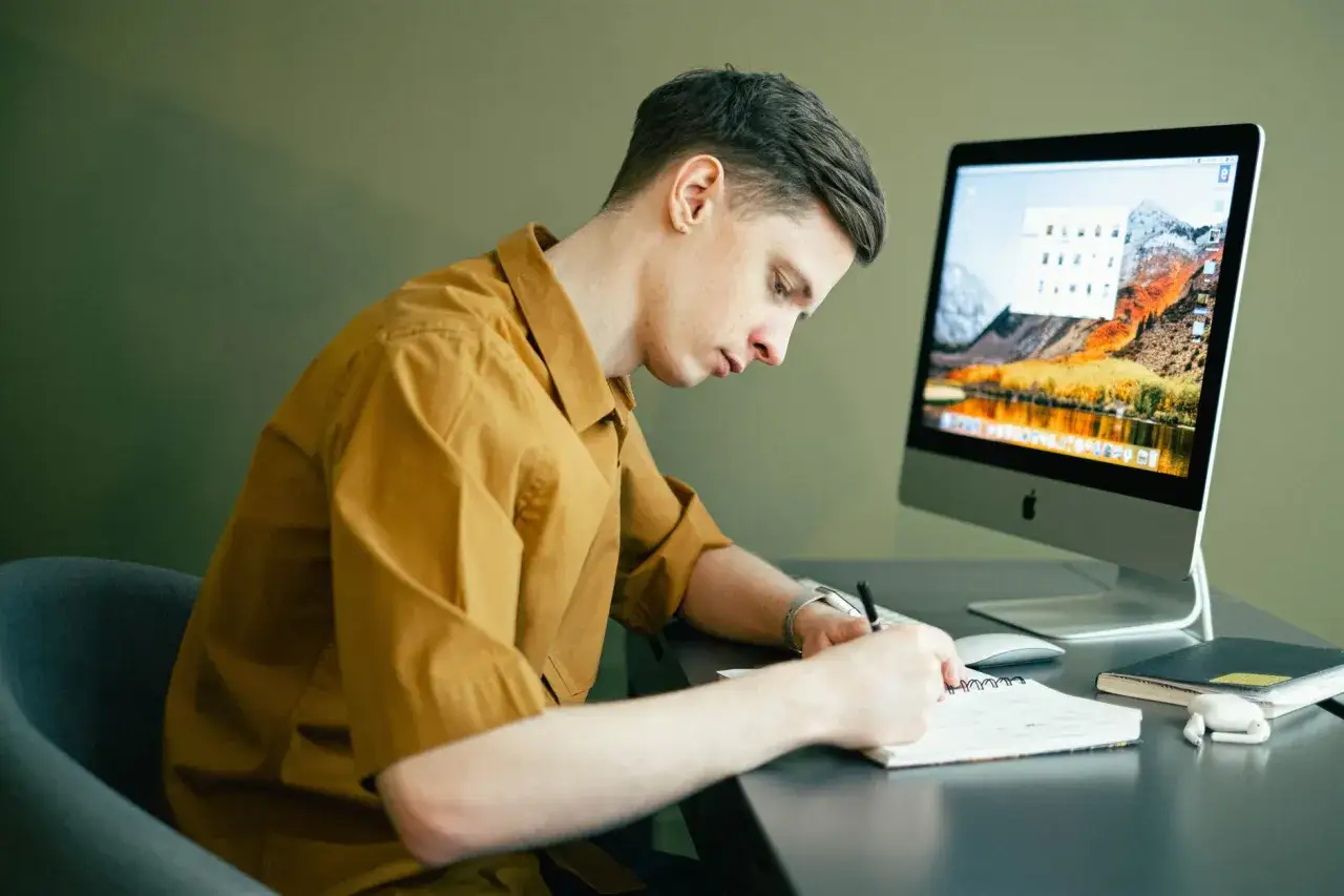 Student pisze notatki, pracując online przy biurku. Elastyczna praca online dla studenta to świetny sposób na zarobek.